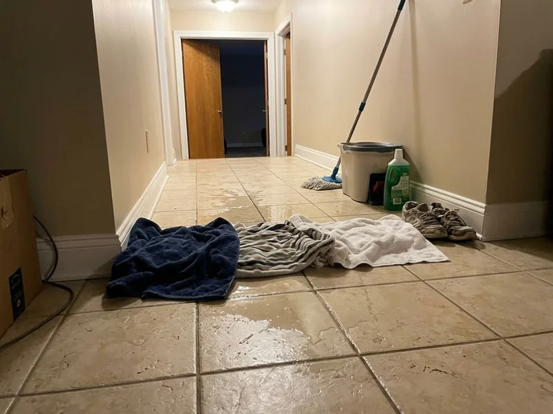 Water spreading across a tile hallway with towels piled against it during an active leak