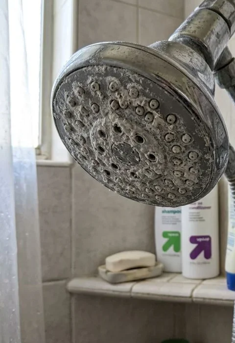 Heavy white mineral scale crusted on a shower head and faucet aerator in an Imperial Valley bathroom