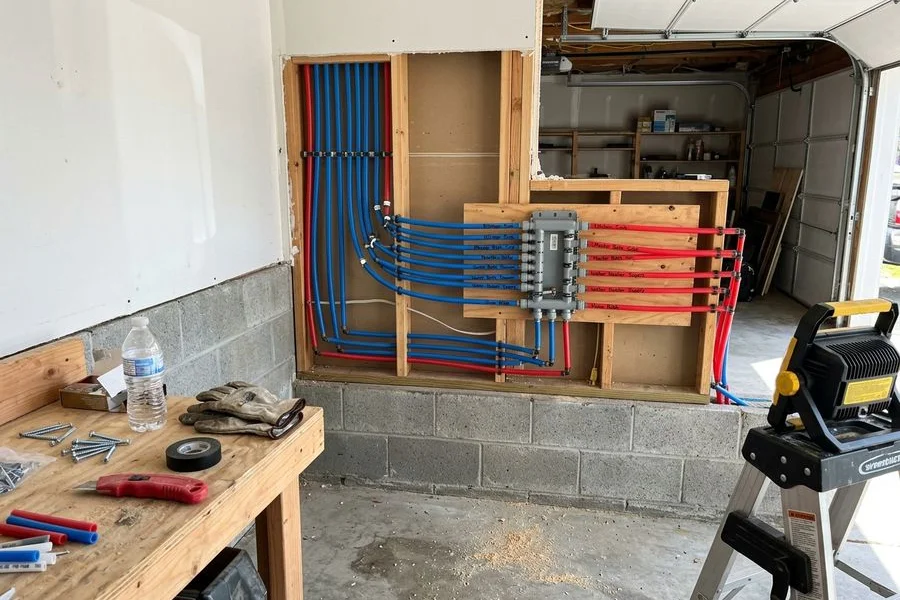 Completed PEX repipe manifold with labeled lines mounted in a garage wall