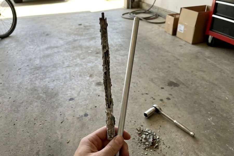 Heavily corroded anode rod held beside a new replacement rod